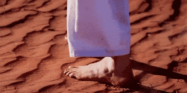 Feet walking over desert sand, wind shaping the desert, feet leaving their temporary imprint.
